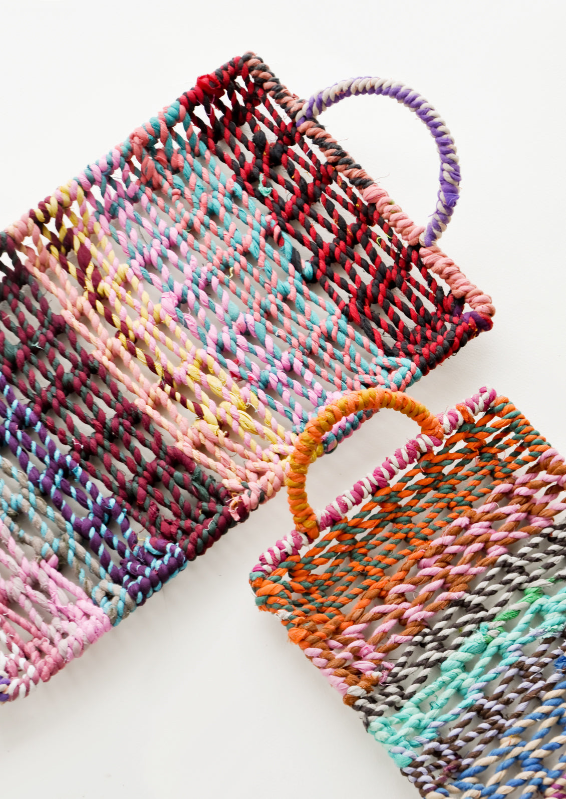 Two differently sized striped multicolor fabric trays with rounded handles. 