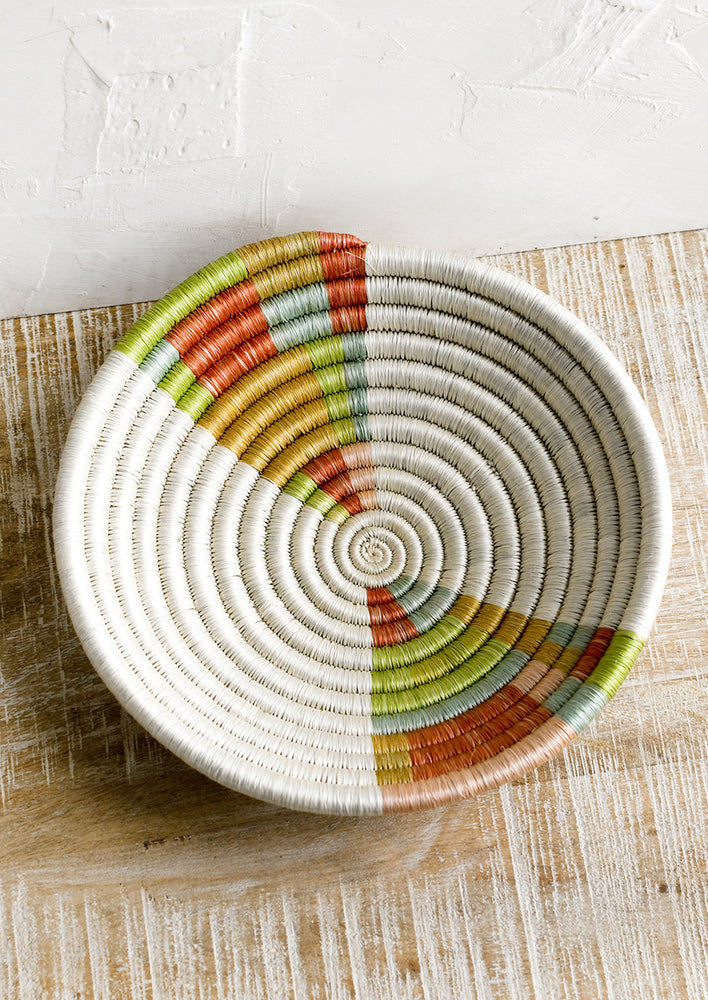A woven sweetgrass bowl in white with multicolor geometric design.