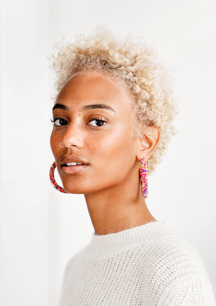 Model wears multicolored beaded hoop earrings and white sweater.