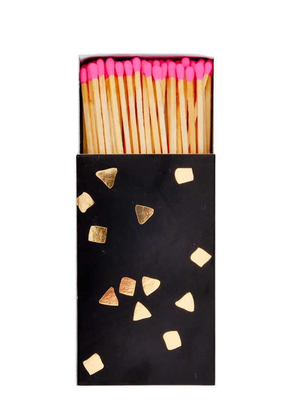 2: A black matchbox with golden flecks is slid open to reveal matchsticks with neon pink tips.