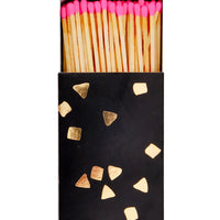 2: A black matchbox with golden flecks is slid open to reveal matchsticks with neon pink tips.