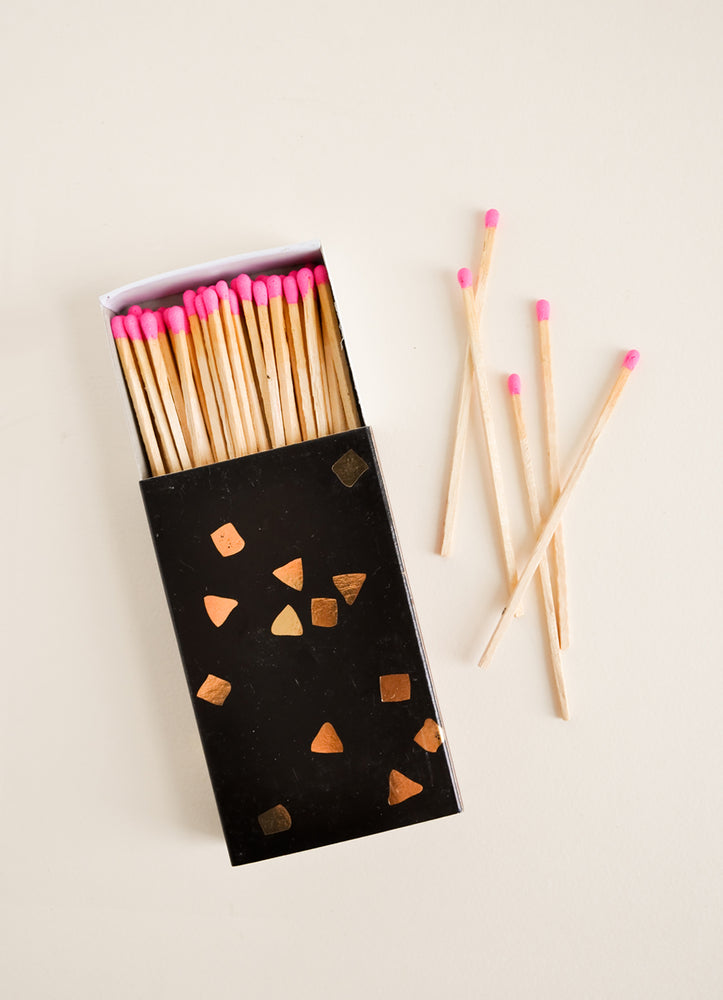 1: A black matchbox with golden flecks is slid open to reveal matchsticks with neon pink tips.