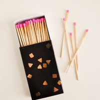 1: A black matchbox with golden flecks is slid open to reveal matchsticks with neon pink tips.