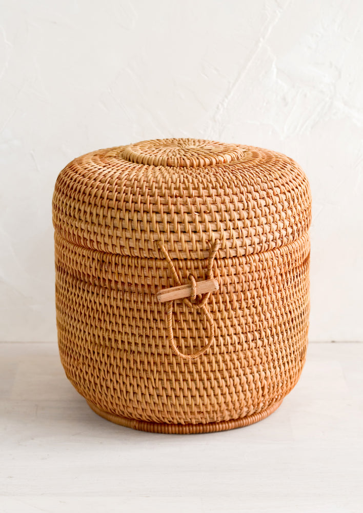 A cylindrical rattan basket with lid and toggle closure.