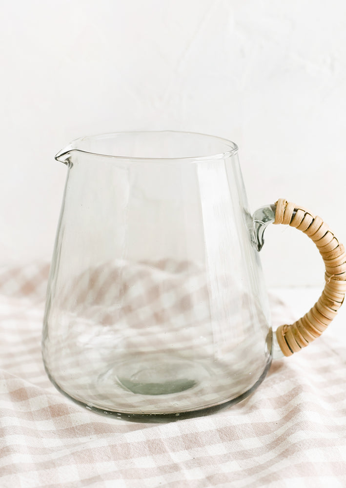 A clear glass pitcher with seagrass wrapped handle.