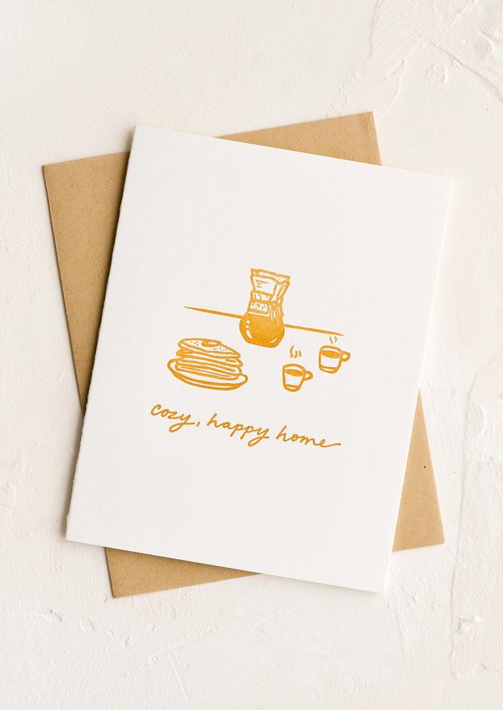 1: A letterpressed greeting card with breakfast scene and text reading "Cozy, happy home".