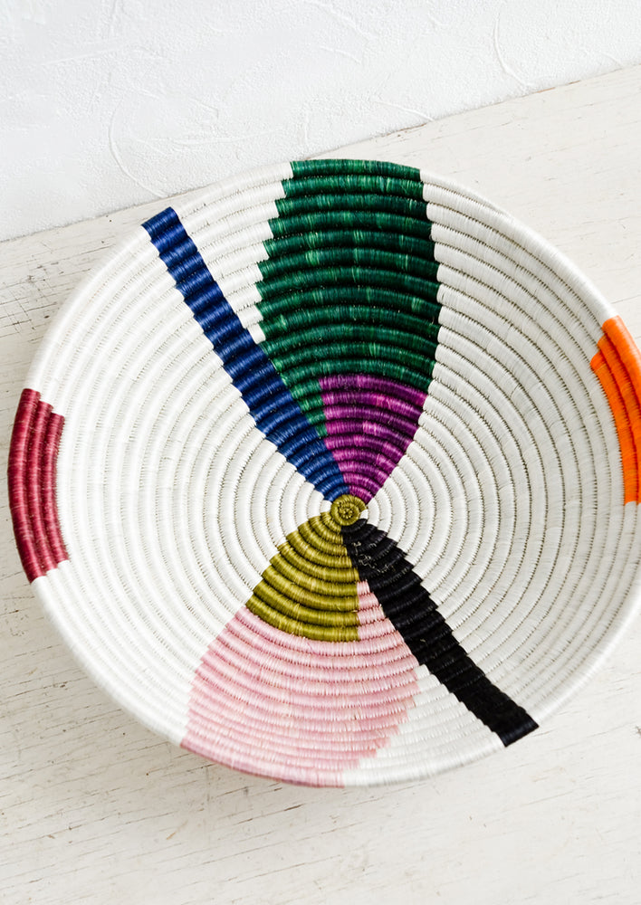 A large woven sweetgrass bowl in white with colorful abstract shapes.