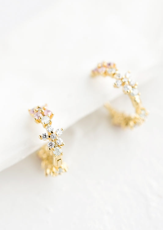 A pair of gold huggie hoop earrings with crystal flowers.