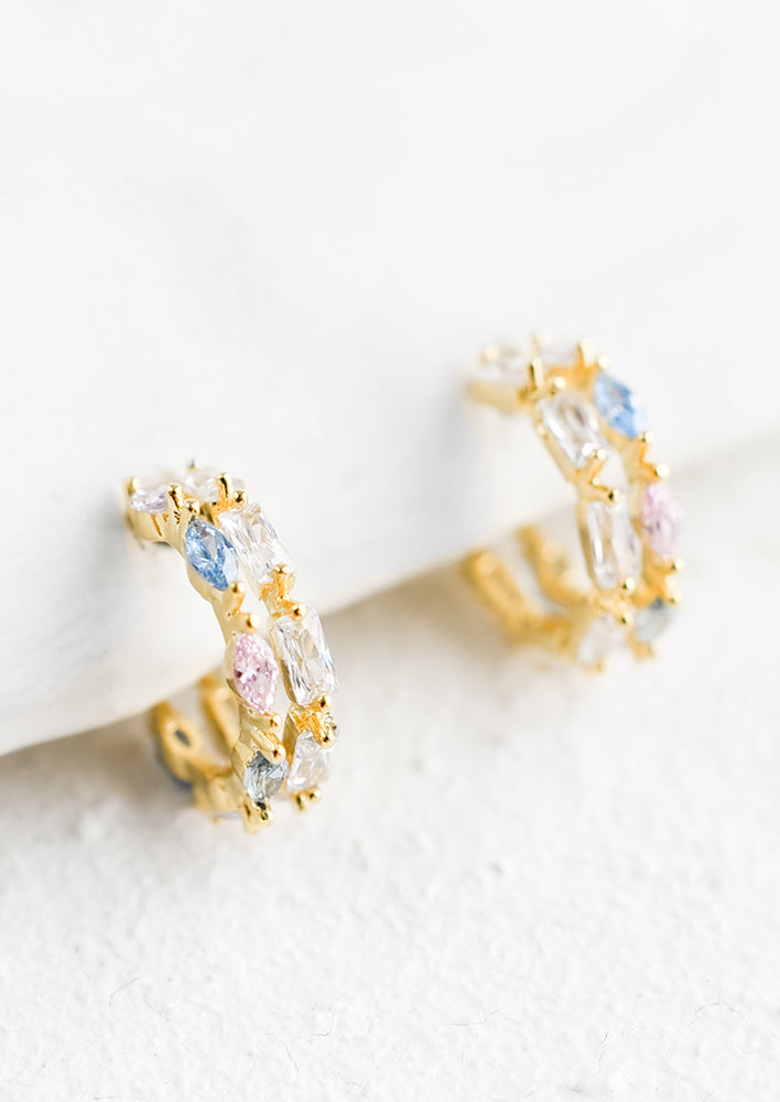 A pair of small gold huggie hoop earrings with clear, pink and blue crystals.