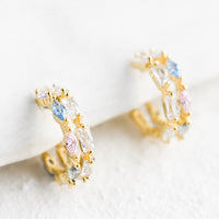 1: A pair of small gold huggie hoop earrings with clear, pink and blue crystals.