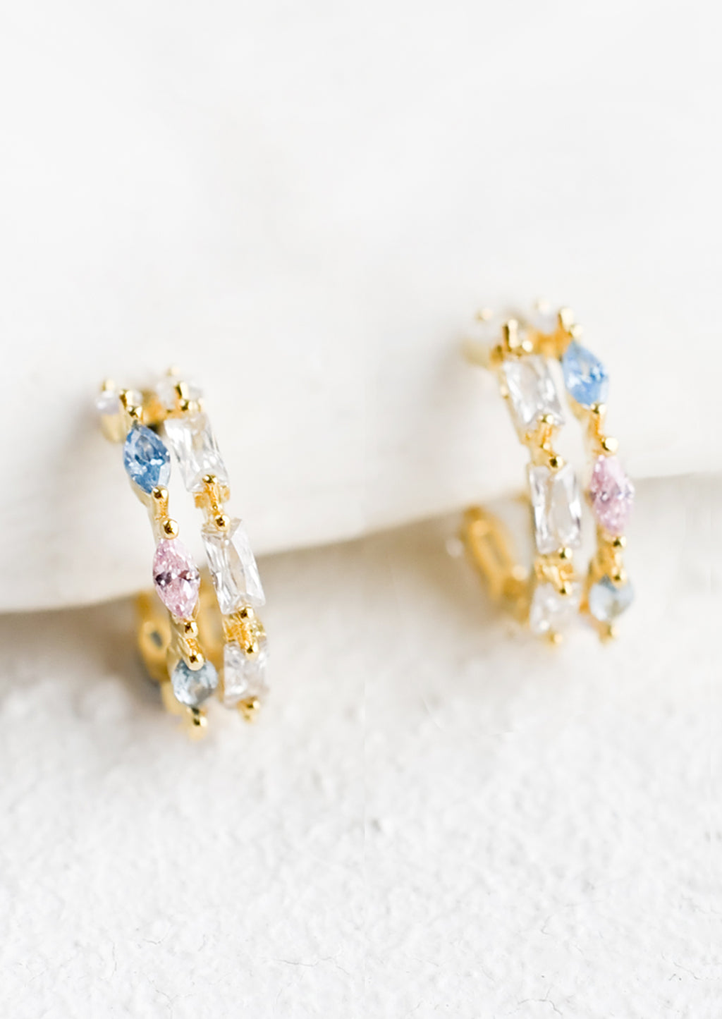 2: A pair of small gold huggie hoop earrings with clear, pink and blue crystals.