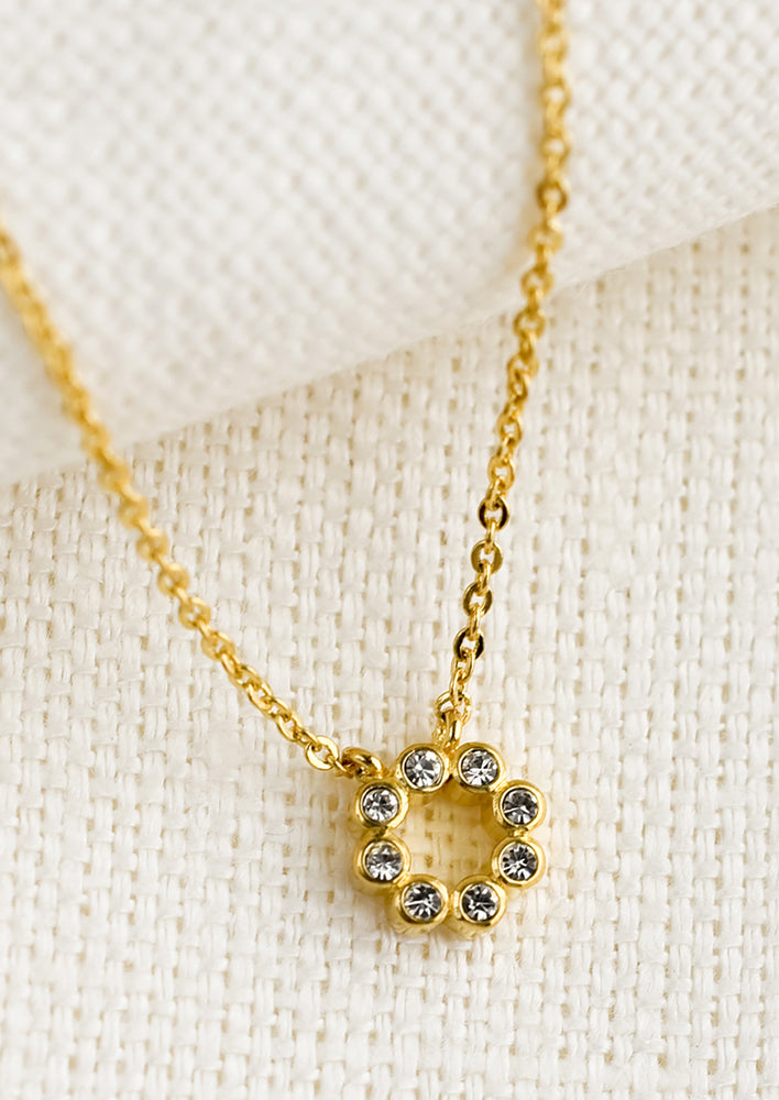 A gold necklace with circular crystal charm.