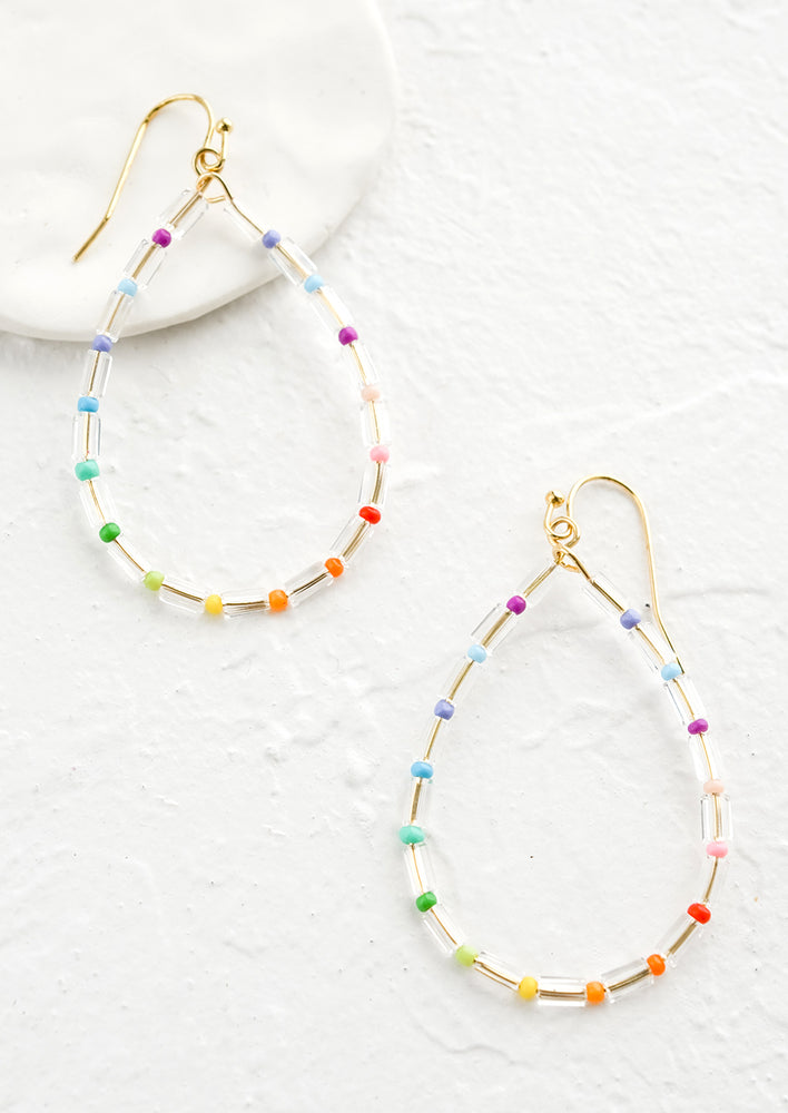 Beaded earrings in oval shape with clear beads alternating with seed beads in rainbow colors.