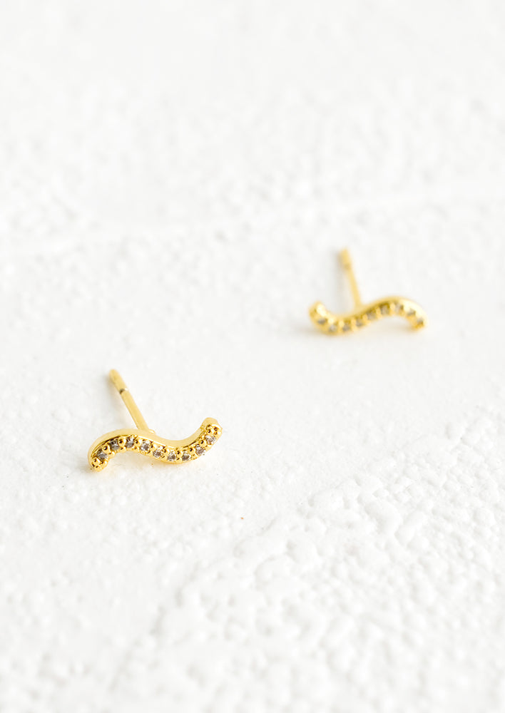 A pair of small gold stud earrings in a squiggle shape with clear crystal embellishment.