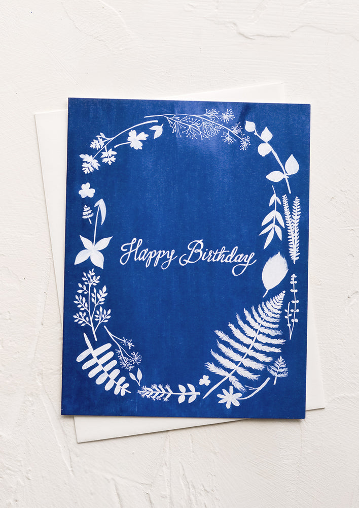 A blue greeting card with white floral print and "Happy birthday" in cursive.