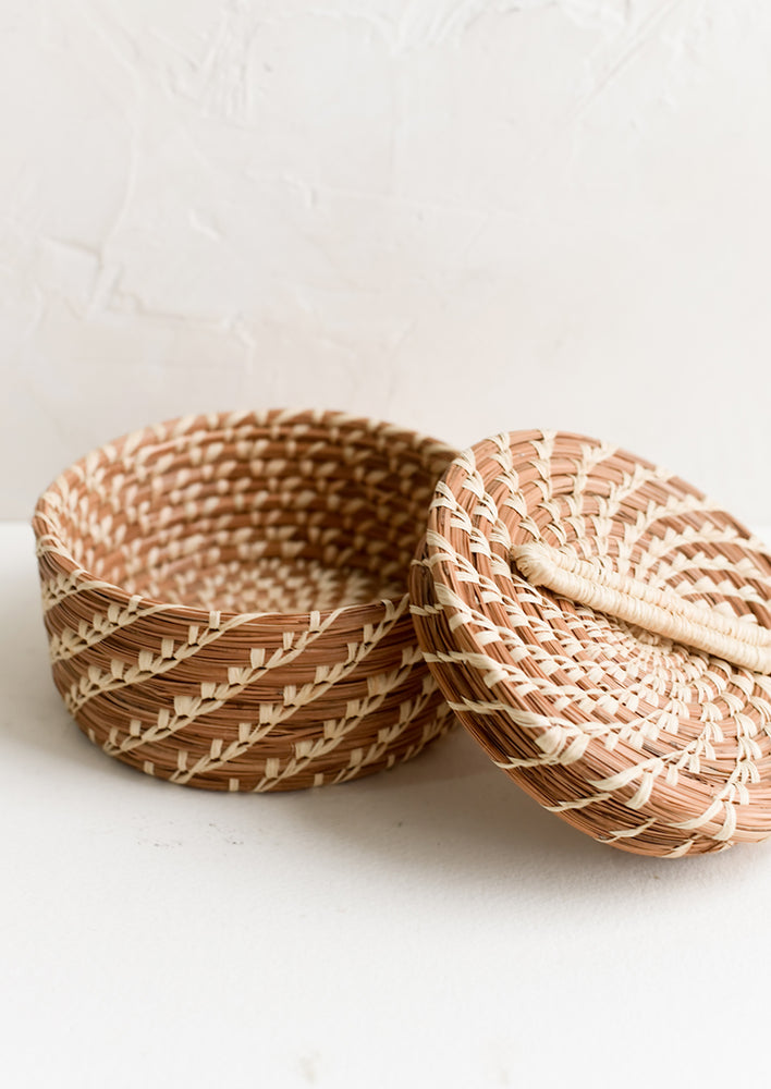 A small, round lidded basket made from woven pine needles.