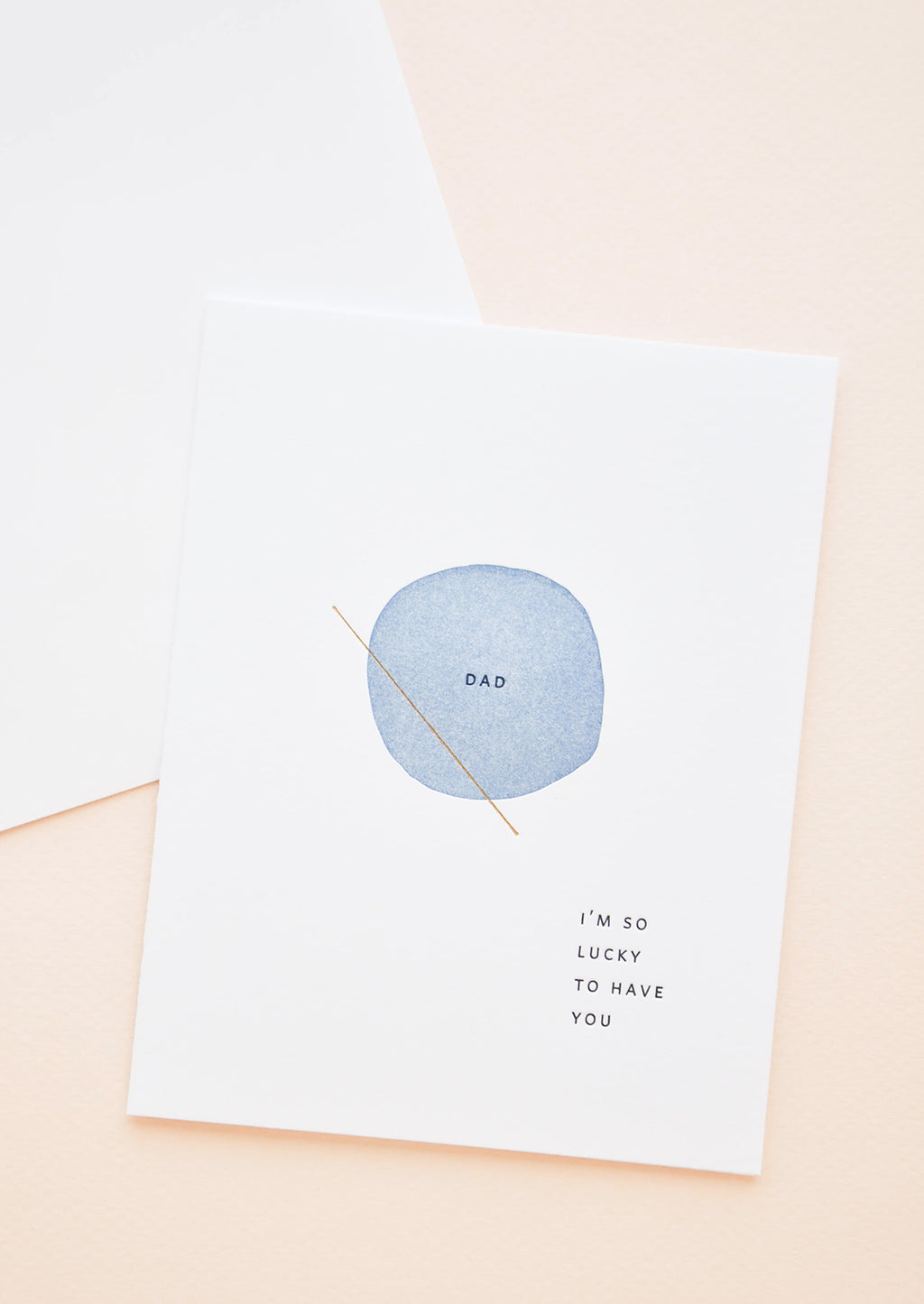 1: White greeting card with letter press printed blue circle at center reading "Dad". Bottom corner reads "I'm So Lucky To Have You".