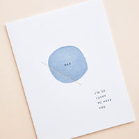 2: White greeting card with letter press printed blue circle at center reading "Dad". Bottom corner reads "I'm So Lucky To Have You".