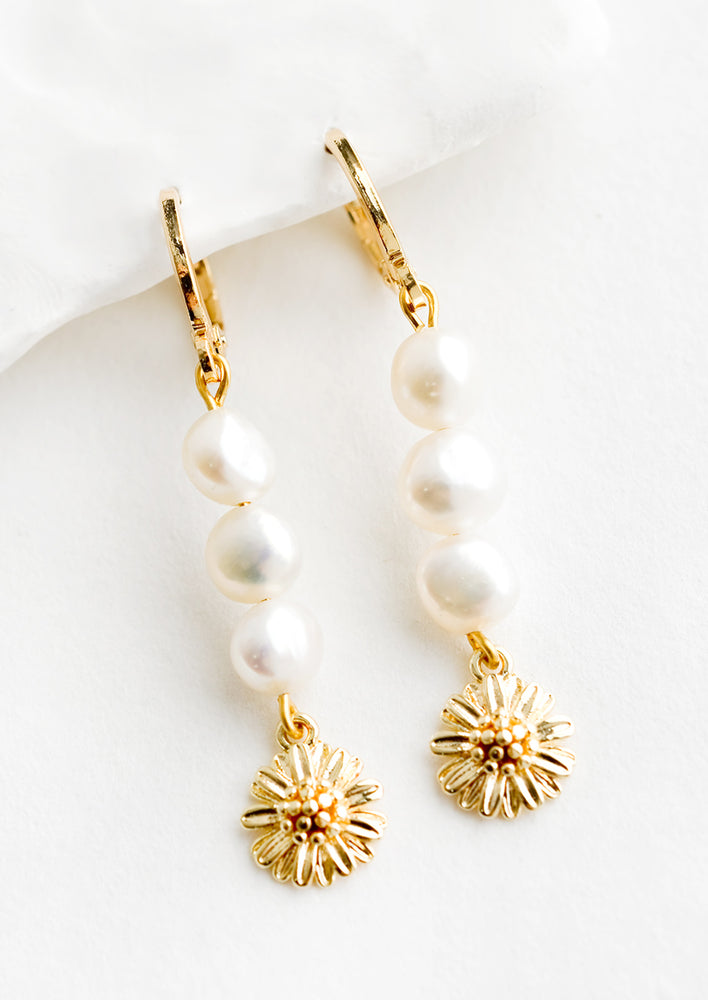 A pair of gold earrings with three pearls and a flower charm at bottom.