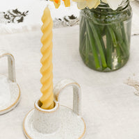 2: A spiral beeswax taper candle in a ceramic holder on table setting.