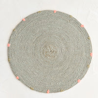 Soft Grey: A round seagrass placemat in grey with grey and pink dashes embroidered around rim.