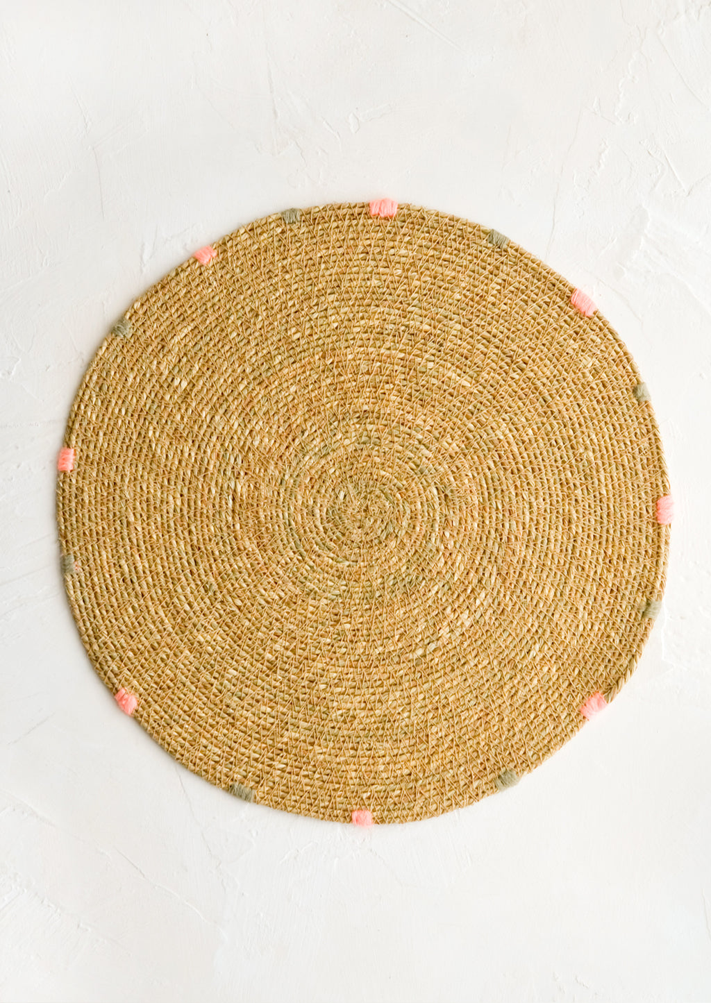 Tan: A round seagrass placemat in natural with grey and pink dashes embroidered around rim.