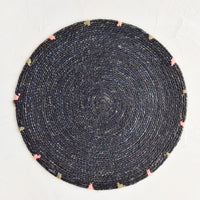 Navy: A round seagrass placemat in navy with grey and pink dashes embroidered around rim.