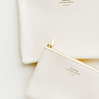 Cream / Small: Medium and small vinyl pouches with gold zipper and crosshatch texture, in cream.