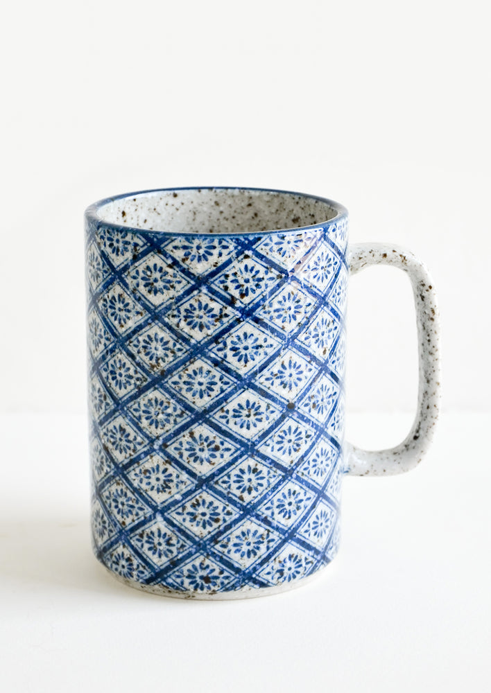 A tall mug with handle made from speckled grey ceramic with diamond indigo tile pattern throughout.