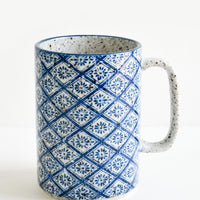 Diamond Floral: A tall mug with handle made from speckled grey ceramic with diamond indigo tile pattern throughout.