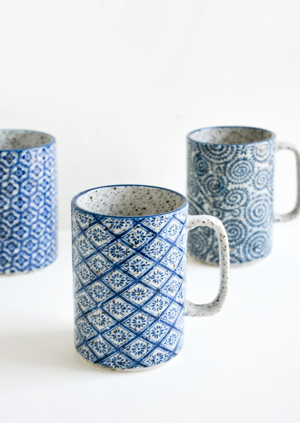 1: Tall ceramic mugs with handles, made from speckled grey ceramic with assorted indigo patterns inspired by Delft pottery.