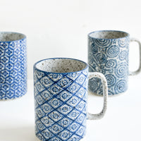 1: Tall ceramic mugs with handles, made from speckled grey ceramic with assorted indigo patterns inspired by Delft pottery.