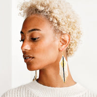 Ivory / Black / Gold: Model wears ivory fringe earrings with black stripe down the center.