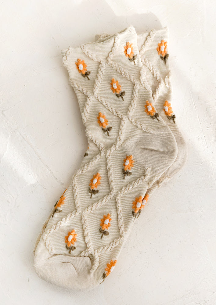 A pair of oatmeal colored socks with raised diamond texture and orange flowers.