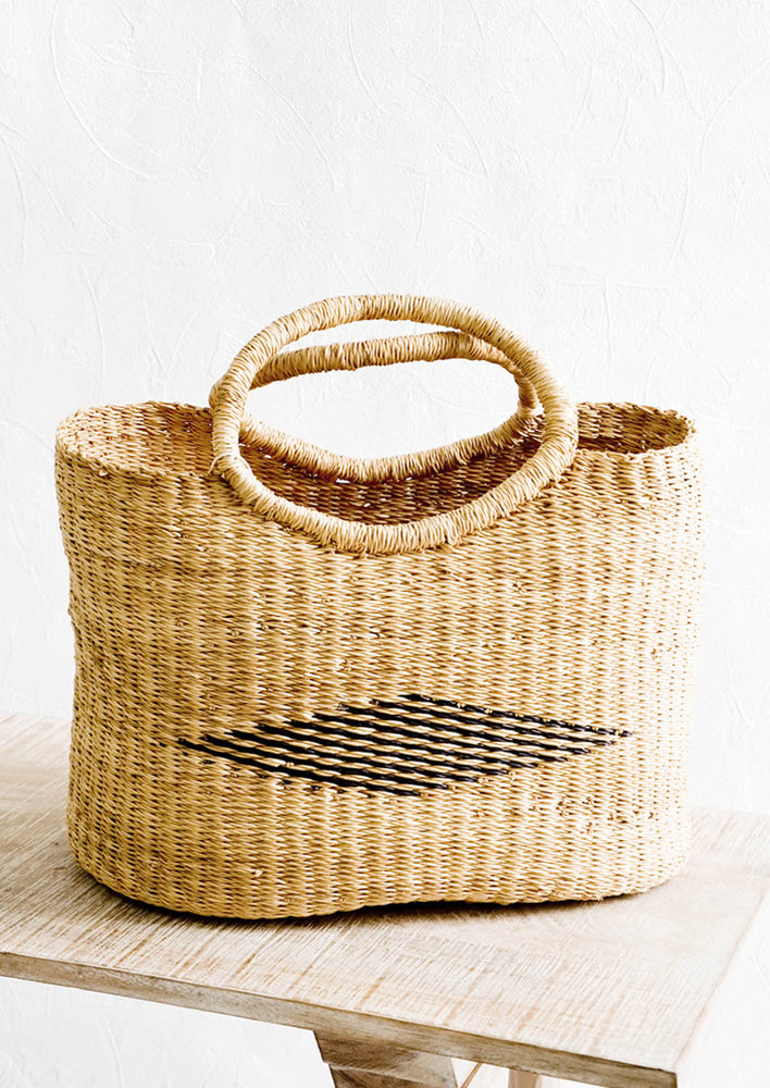 Woven tote bag made from natural elephant grass. Black diamond pattern woven at center, two handles at top.