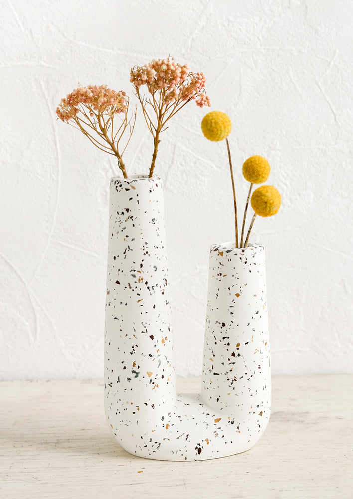 A u-shaped tubular vase made from white concrete with terrazzo flecks.