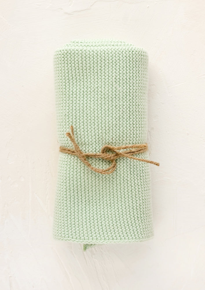 A knit cotton dish towel in mint, rolled and tied with twine.