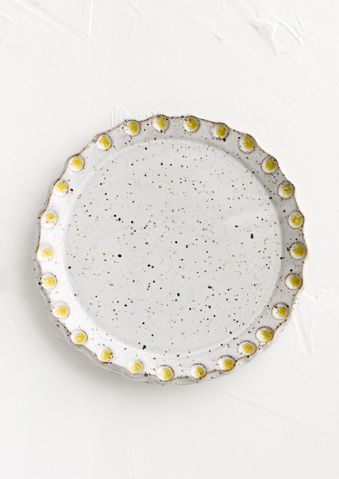A round ceramic plate with yellow dot print detail.