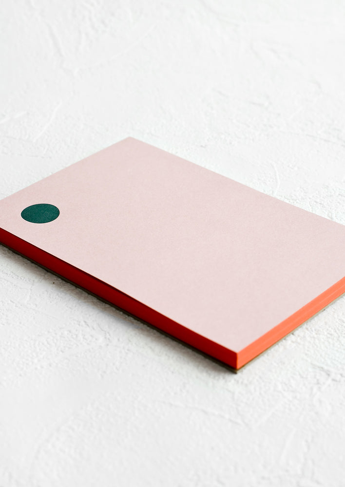 A pink notepad with green dot at top left corner and red painted edges.