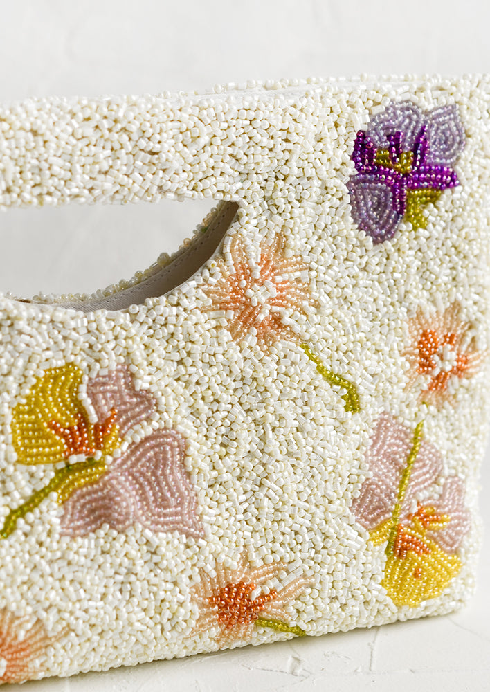 2: A white beaded east-west clutch with cutout handle and pastel floral pattern.
