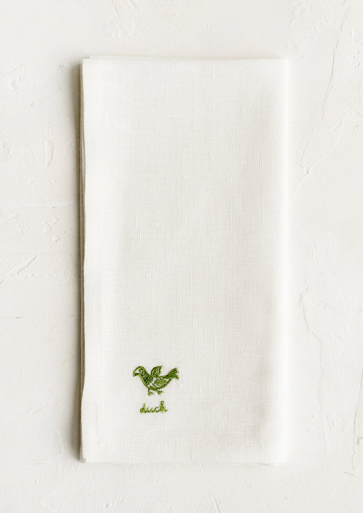 An ecru linen napkin with green embroidered duck and "duck" text embroidered in green at corner.