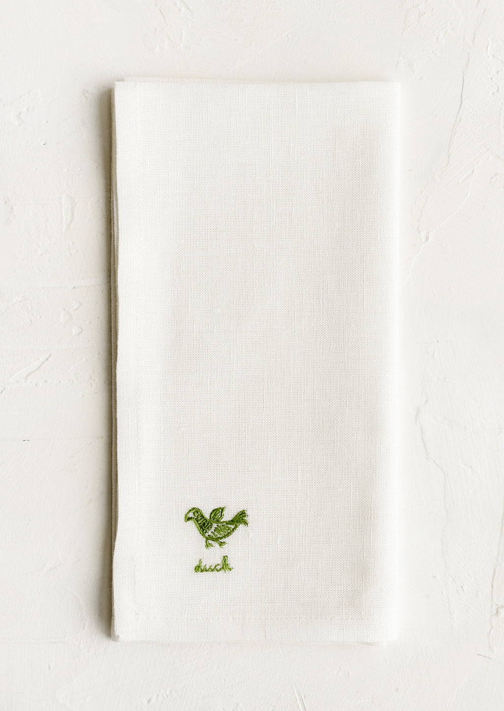 2: An ecru linen napkin with green embroidered duck and "duck" text embroidered in green at corner.