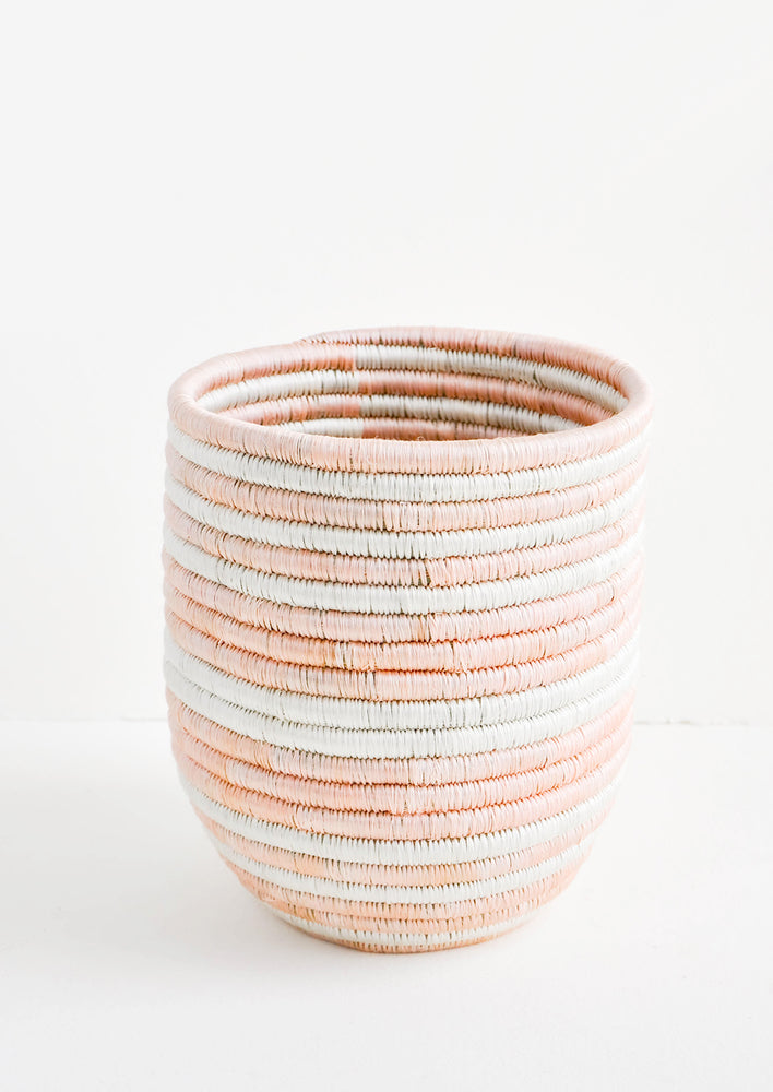 1: Elongated, round basket woven out of dyed sweetgrass in alternating light pink and white stripes.