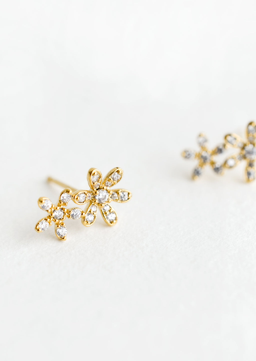 2: A pair of gold stud earrings in a two flower silhouette with clear crystal detailing.