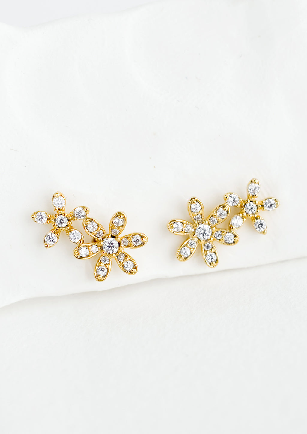 1: A pair of gold stud earrings in a two flower silhouette with clear crystal detailing.