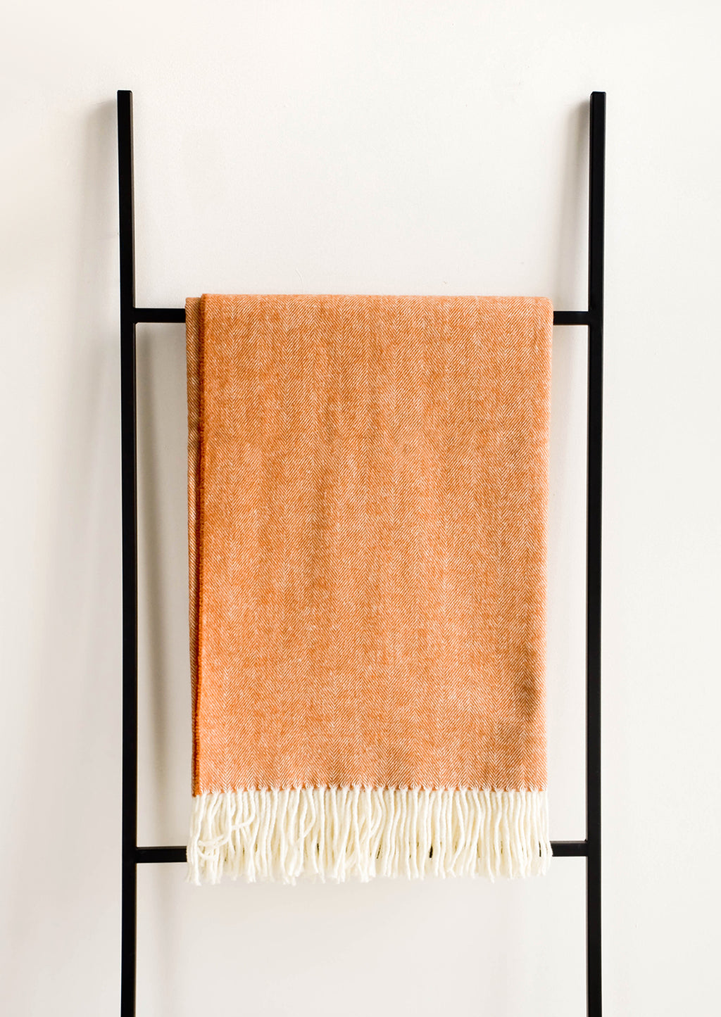 3: Soft blanket in colored herringbone weave. Ivory tassel trim at ends. Displayed hanging on a ladder.