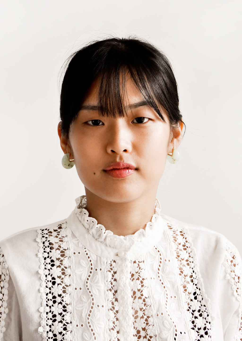 2: Model wears green gemstone earrings and white blouse.