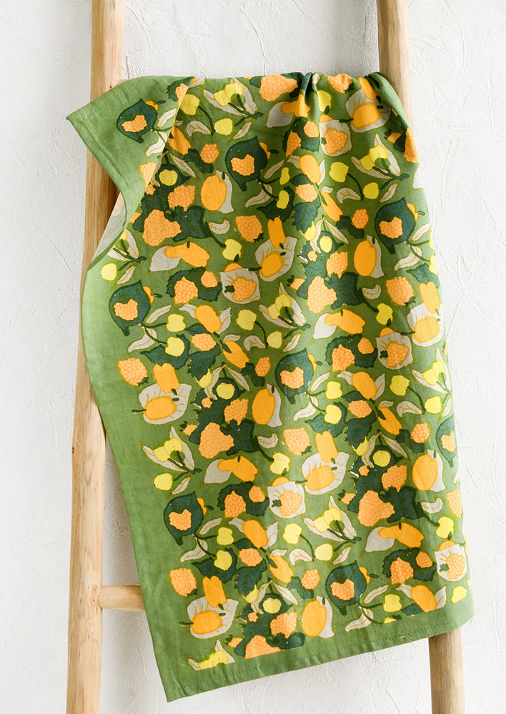 A fruit printed tea towel in green, orange and yellow color palette.