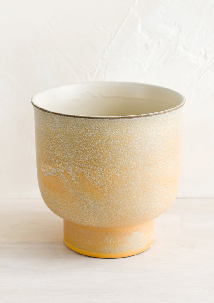 A ceramic planter with footed silhouette in mottled tan glaze.