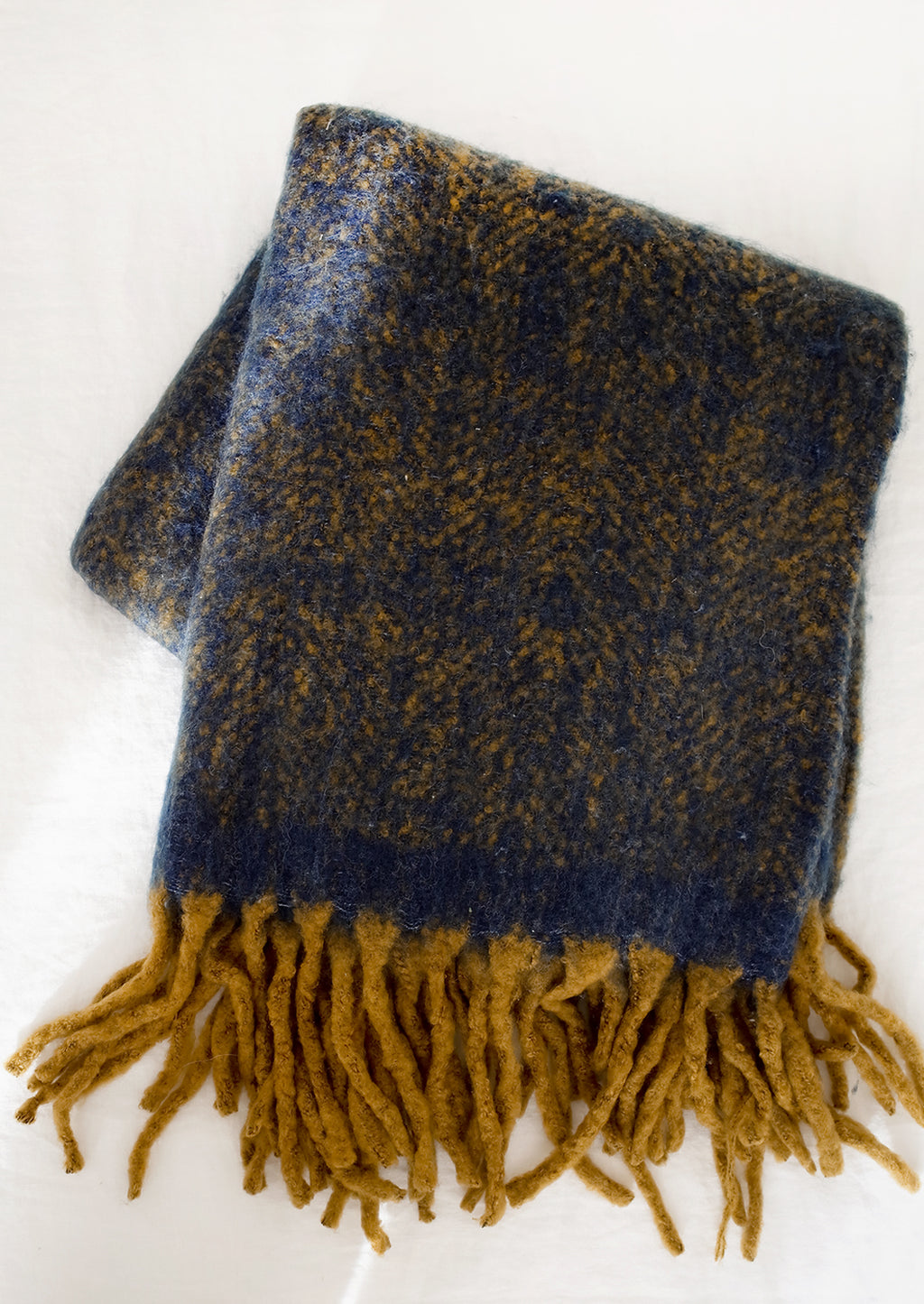 2: A fuzzy mohair-like blanket in navy and mustard with mustard tassel trim.